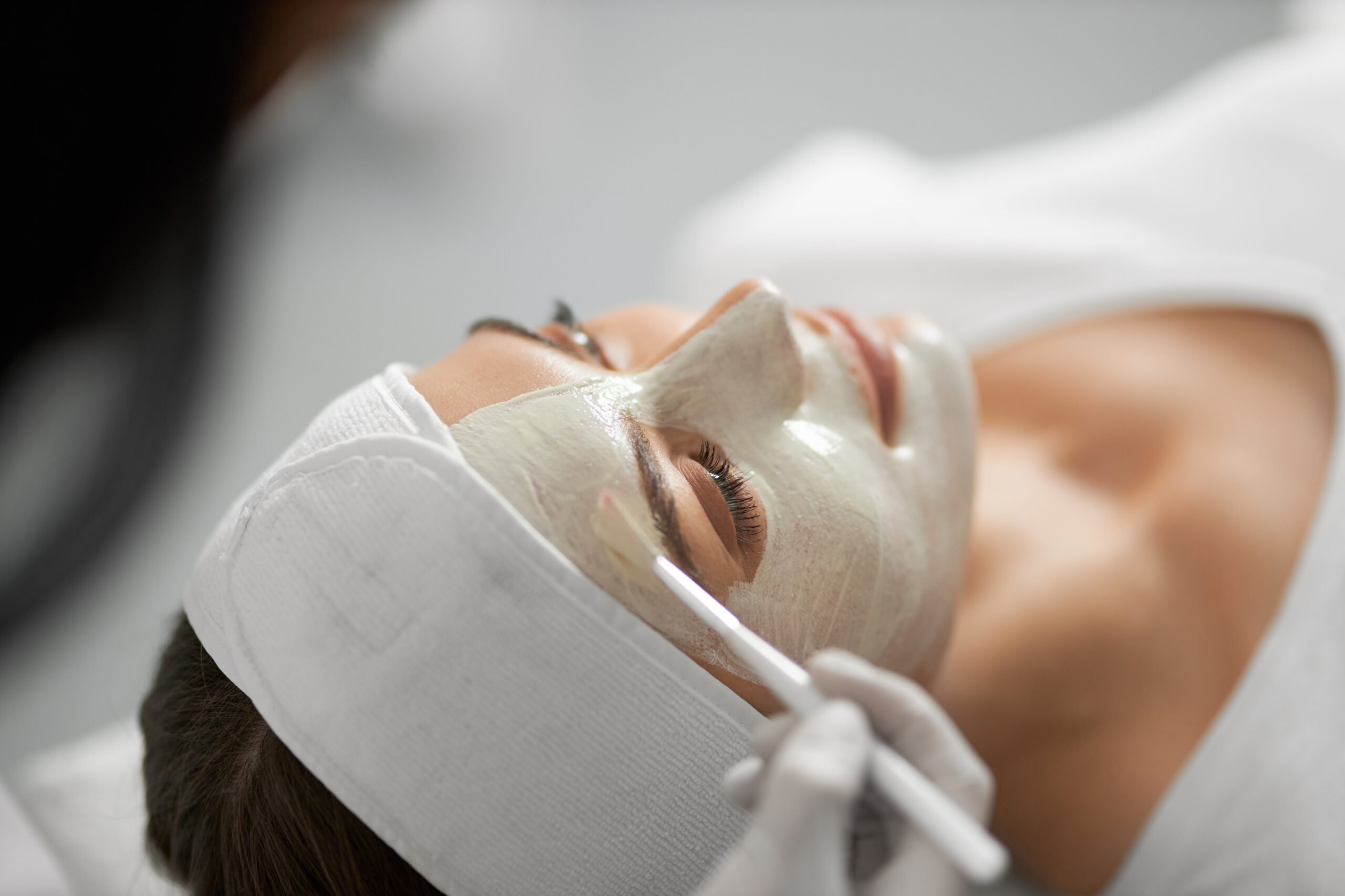 Side view of young beautiful woman lying on procedure for skin rejuvenation in professional beauty salon. Concept of white mask for face with special useful components for skin.